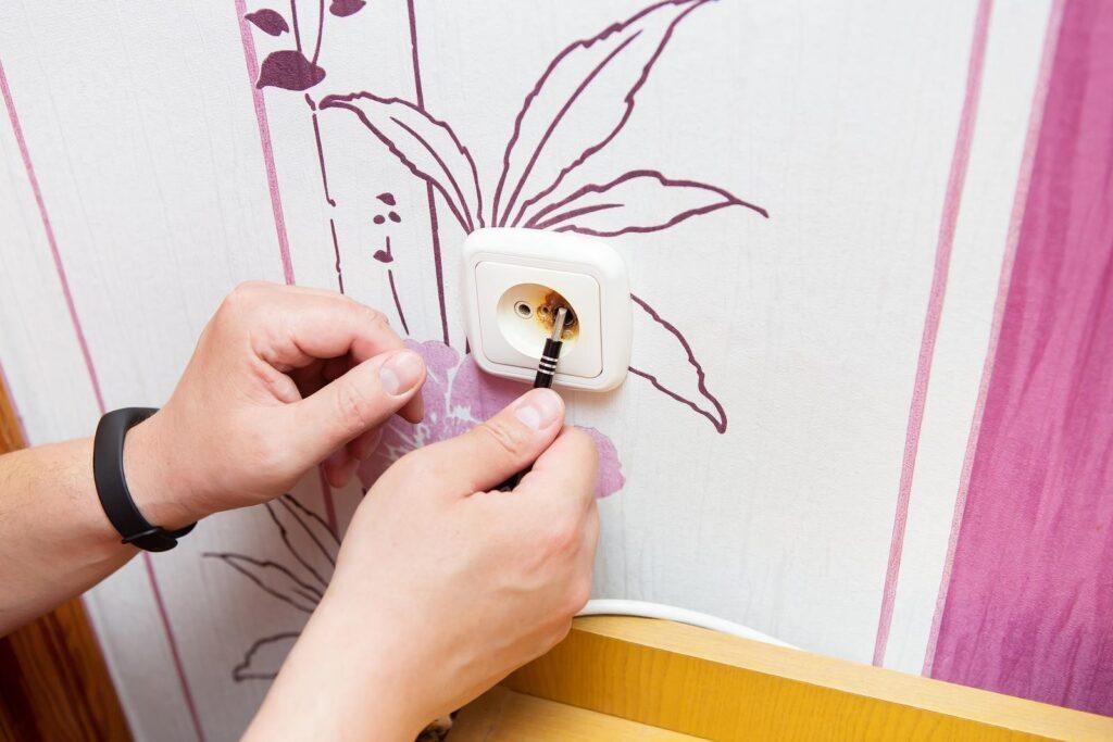 Hands installing wallpaper around power outlet.